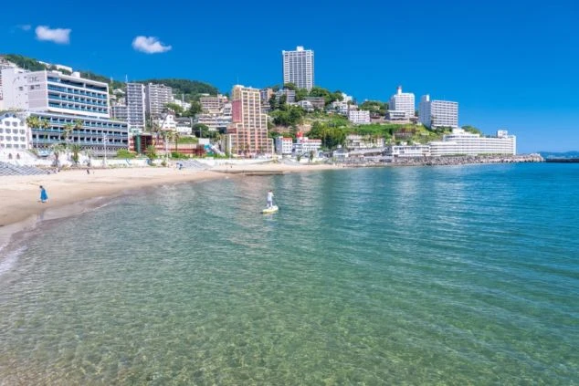 青い海と白い砂浜が広がる熱海サンビーチで、サップ（SUP）を楽しむ人の画像。