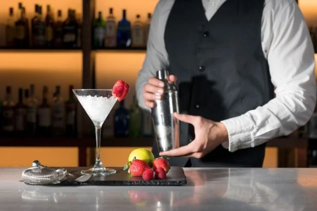 バーカウンターでバーテンダーがシェイカーを振り、カクテルを作っている手元の画像。