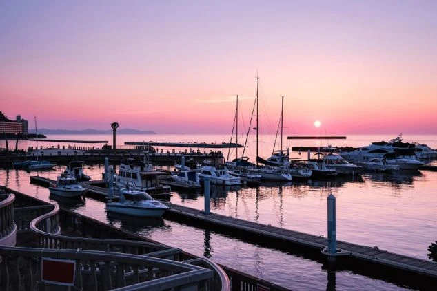 高台から見下ろす、青い海と山々に囲まれた熱海の街並みの全景の画像。