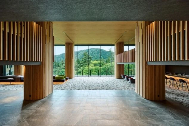 木目調のルーバー装飾が施された柱が並ぶ、開放的なロビー。正面の大きな窓からは豊かな緑の山が見える。