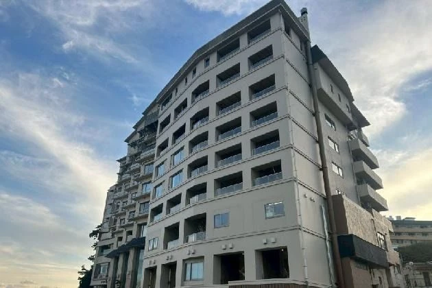 夕暮れ時の青空を背景に、ベランダが規則的に並ぶ多層階の白い大型ホテルの外観を斜め下から見上げた様子。