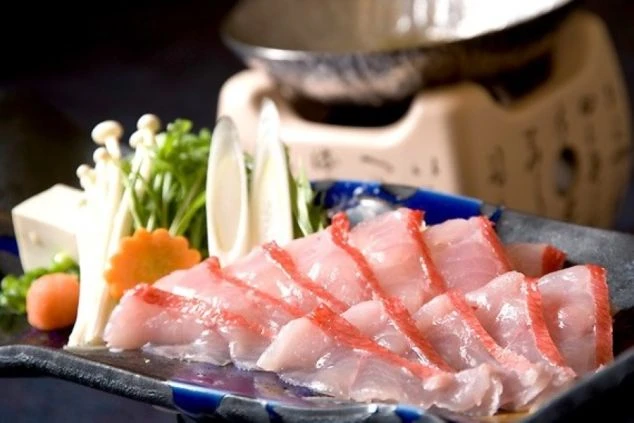 鮮やかな赤い縁取りが特徴的な金目鯛の刺身。背景にはえのきや豆腐などの鍋の具材と、卓上コンロが見える。