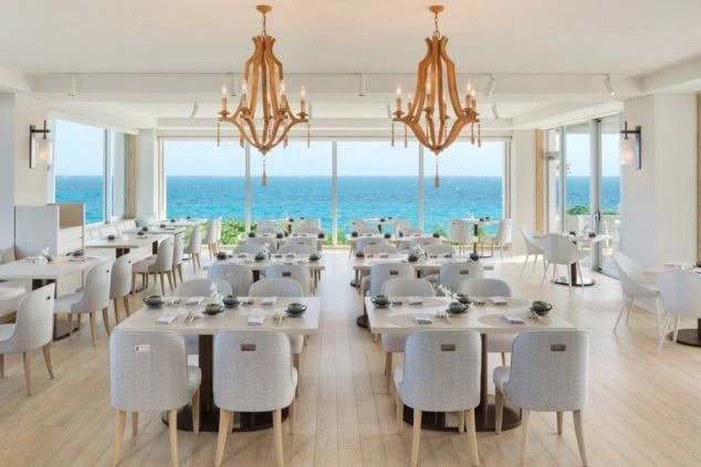 大きな窓から青い海を一望できる、白を基調とした明るいレストラン。天井からは木製のお洒落なシャンデリアが吊るされている。