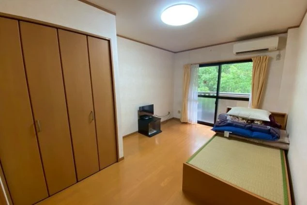 畳敷きのベッド、木目調のクローゼット、テレビがある、白を基調としたシンプルな個室。