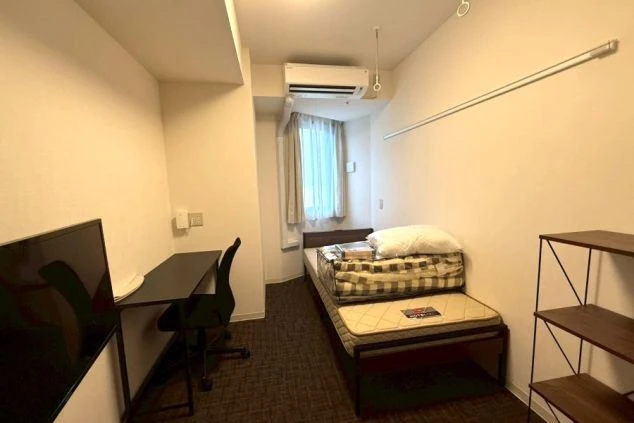 ベッド、デスク、棚が配置された洋室の全景。