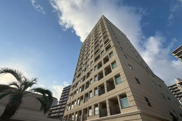 青空を背景に見上げる、モダンな高層マンションの外観。