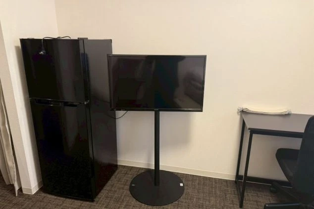 黒い冷蔵庫、薄型テレビ、デスクがある部屋の一角。