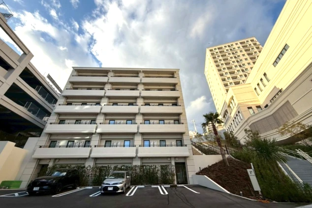 駐車場越しに見える、白いバルコニーが並ぶモダンなマンション外観。