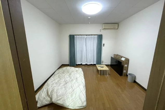 リゾートバイトの個室寮の内観。フローリングの部屋に布団、ローテーブル、テレビ、エアコンが完備された、シンプルで清潔な住み込み生活のプライベート空間。