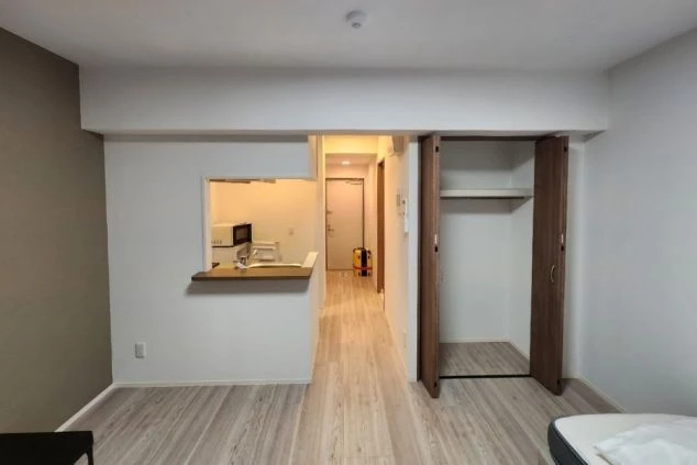 白い壁と明るい木目調の床のシンプルな部屋で、奥に別の部屋が見える。