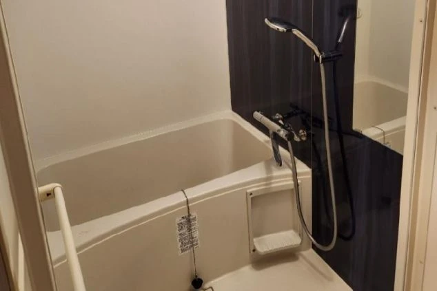 白い浴槽とシャワー、紺色の壁が特徴のシンプルなユニットバス。