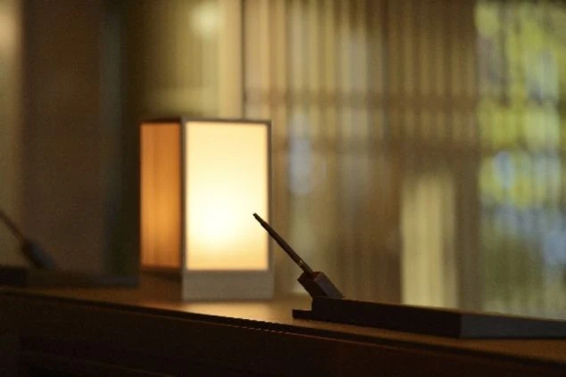 温かいオレンジ色の光を放つ四角い和風の間接照明と、その手前に置かれた筆記具のアップ。背景は柔らかくぼけている。