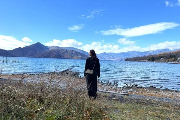 澄み渡る秋の中禅寺湖畔で、雄大な山々を眺めながら静かに佇むスタッフの背中