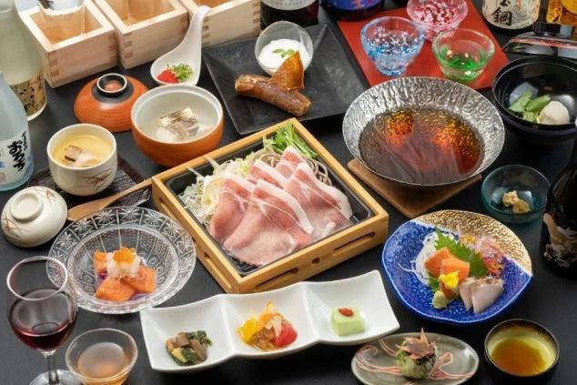 黒いテーブルに並ぶ豪華な和食会席料理。豚肉のしゃぶしゃぶ、お造り、蒸し物、小鉢など、多彩な料理が色鮮やかな器に盛り付けられている。