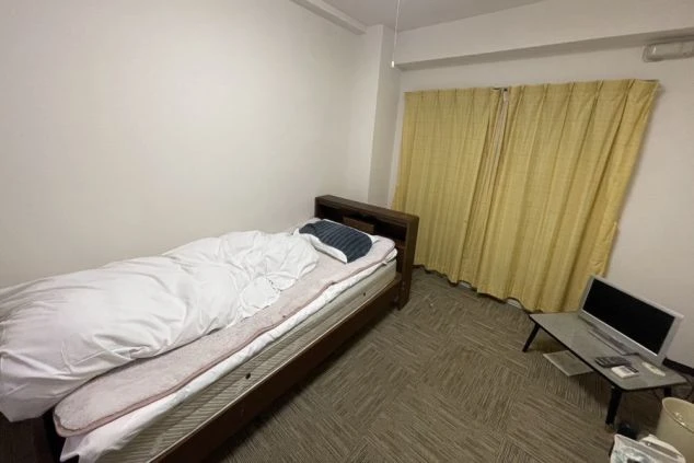 リゾートバイトの個室寮の部屋。シングルベッドとテレビが備え付けられたプライベート空間。一人暮らしに十分な広さの洋室。