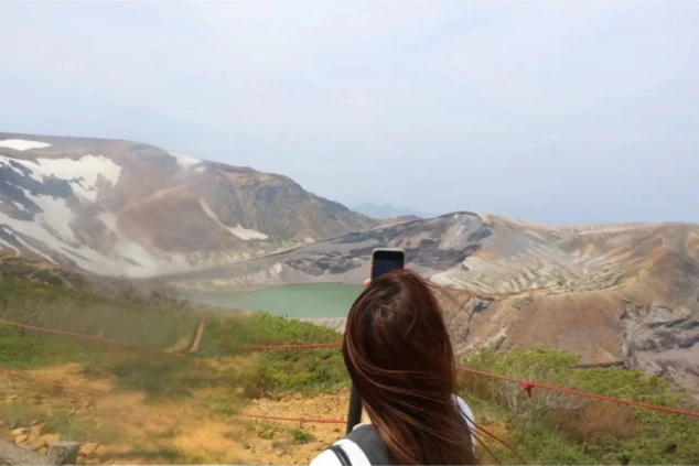 山の頂からスマートフォンで撮影する、エメラルドグリーンの御釜。