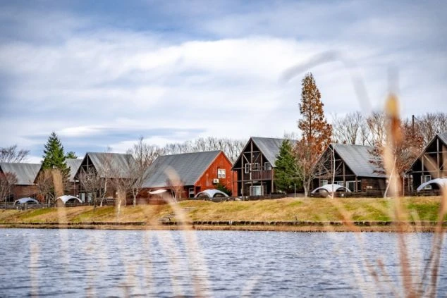 穏やかな湖の向こうに並ぶ、三角形の屋根をした木造コテージ群。
