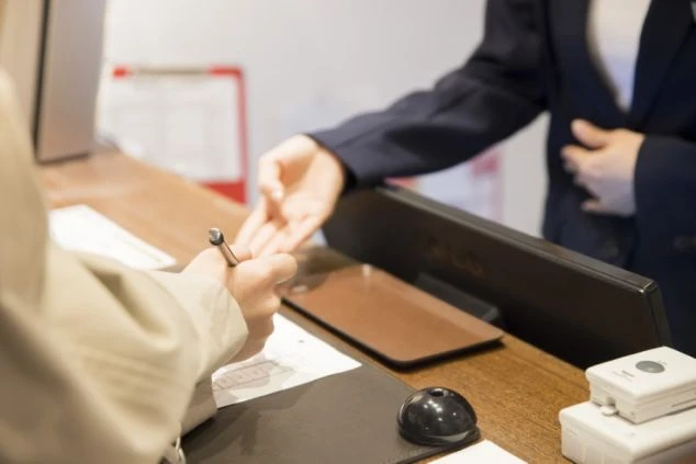 ホテルのカウンターで、スタッフの案内を受けながら記帳する客の手元。