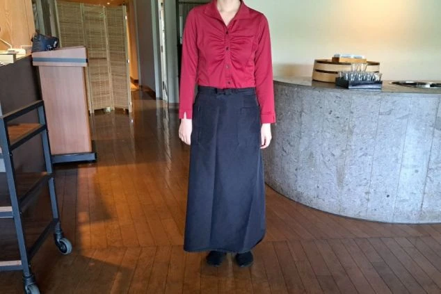 レストラン・フロントで働く女性スタッフの制服。上品なワインレッドのシャツに、黒いロングサロンエプロンを合わせた、落ち着いたスタイルです。