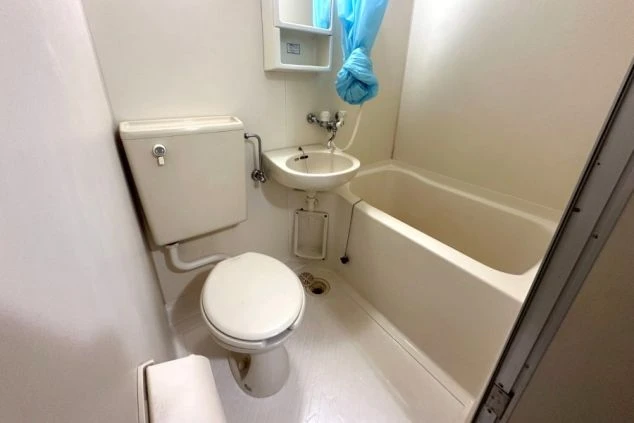 寮のユニットバス。浴槽、シャワー、トイレ、洗面台が一体となった清潔な空間が映る。