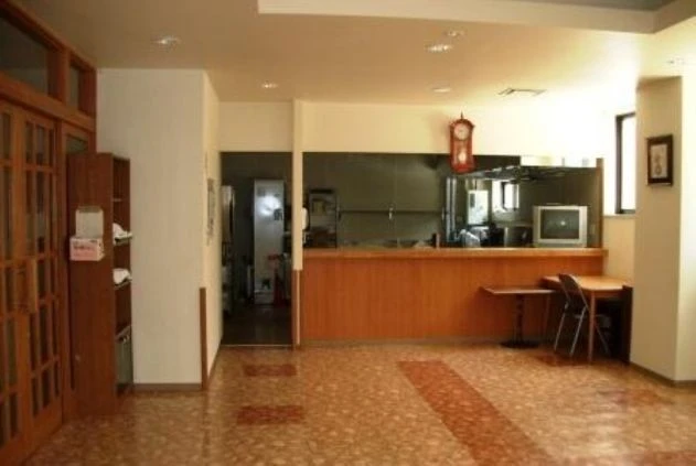 木目調のカウンターがある広々とした食堂。奥には厨房が見え、壁には振り子時計が掛かっている。手前にはテーブルと椅子が配置されている。