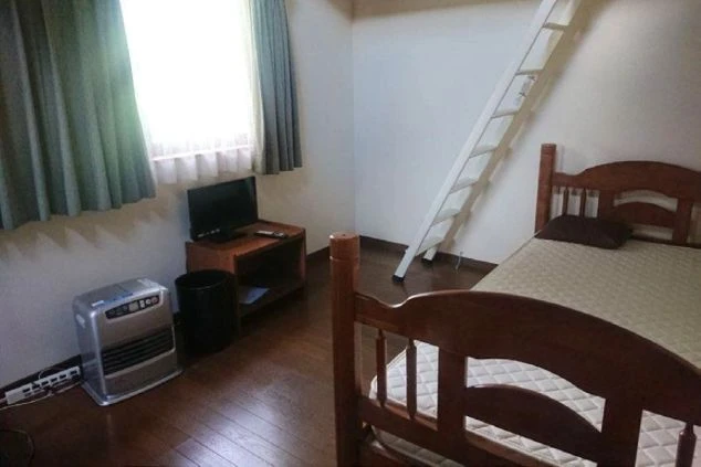 フローリングの洋室。シングルベッドが置かれ、壁にはロフトへ続く白い梯子が掛かっている。窓際にはテレビと小型ヒーターが備わっている。