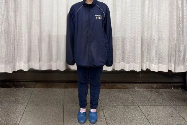 左胸に「STAFF」の文字が入った、ネイビーのジップアップジャンパーを着用したスタッフの制服。下はスリムなパンツと青いサンダルを合わせている。