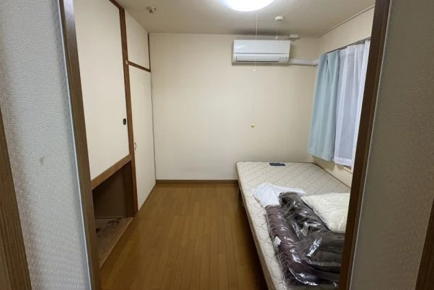 寮にある寝室スペース。エアコン完備で、ベッドや収納スペースが整った快適な1R(ワンルーム)個室。