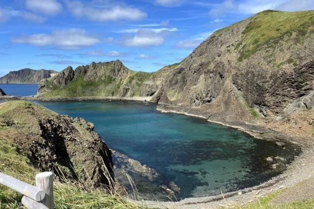 荒々しい断崖絶壁に囲まれた、透明度の高いエメラルドグリーンの入り江。晴天の下、複雑な地形の岩肌と穏やかな海面が美しい自然の風景。