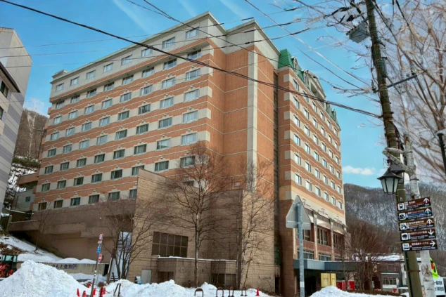青空の下にそびえ立つ北海道の大型リゾートホテル外観。周辺には雪が残り、冬の住み込みバイトの拠点となる建物