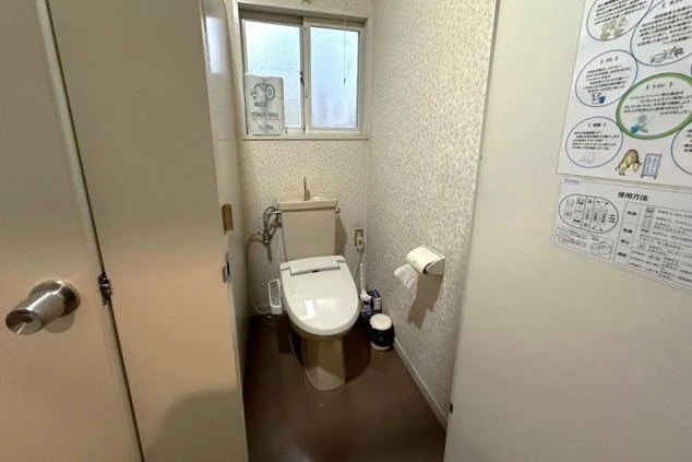 清潔感のある洋式トイレ。温水洗浄便座が完備されており、壁にはトイレットペーパーホルダーや使用方法の案内掲示板が設置されている。