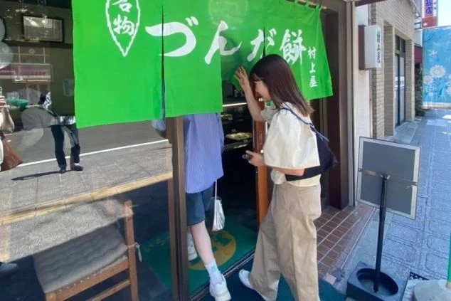 「づんだ餅」と書かれた緑の暖簾をくぐり、店に入る女性。