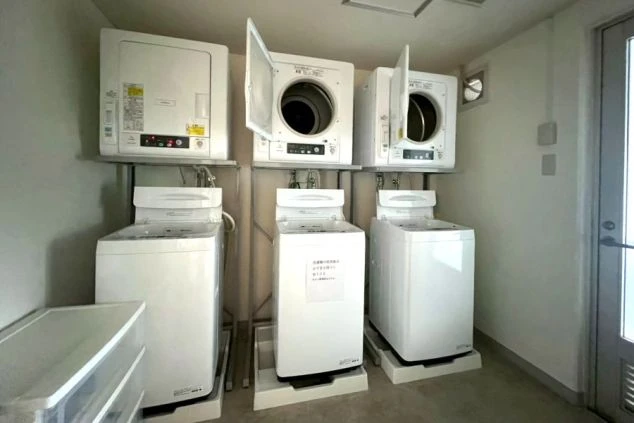 3台の全自動洗濯機と衣類乾燥機が並ぶ、広々としたリゾートバイト寮のランドリー。清掃が行き届いた明るい共有スペース。