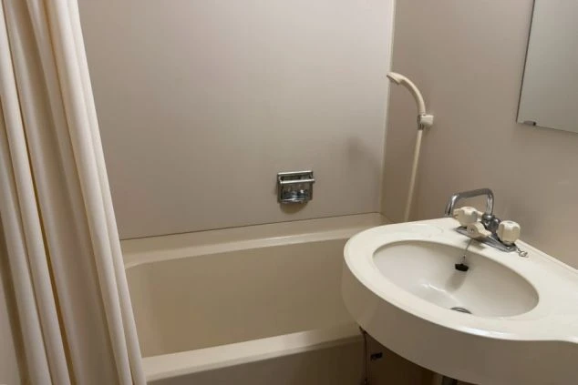 寮のユニットバス。シャワーカーテンと浴槽が備え付けられた浴室。仕事の疲れを癒せる設備。