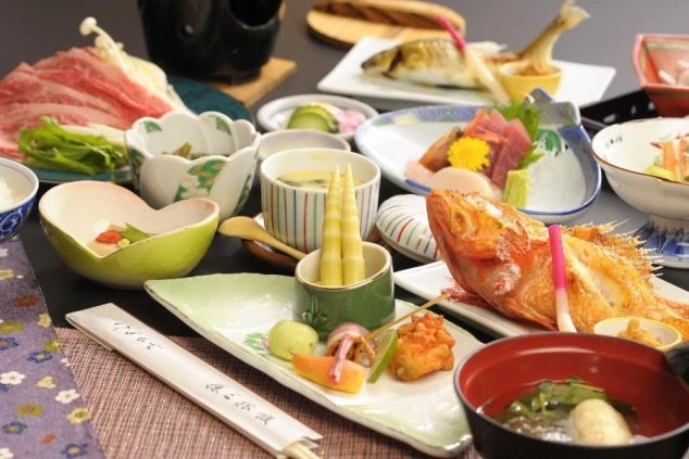 色鮮やかで豪華な会席料理の数々。焼き魚、お造り、煮物、牛肉のしゃぶしゃぶなどが美しい器に盛り付けられ、旬の食材を贅沢に楽しめる和食膳。