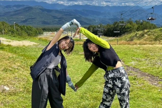 山々を背景に、リフトのある草原でハートポーズを作る2人の女性。