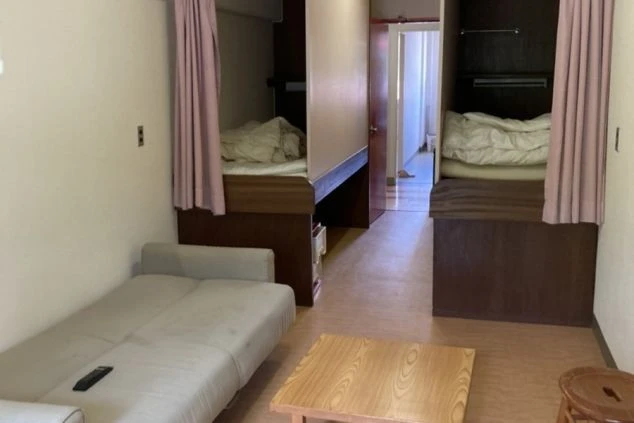 リゾートバイトの寮の部屋の画像。カプセルホテルのようなベッドが並び、テーブルとソファもある。