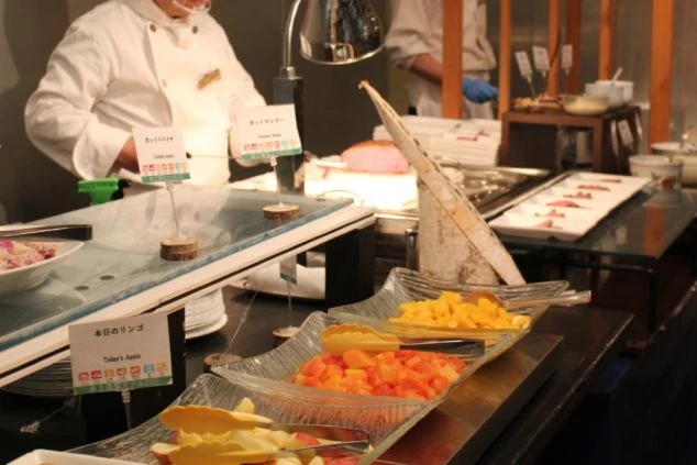 ライブキッチンでシェフが料理を取り分け、手前にはカットフルーツが並ぶビュッフェ。
