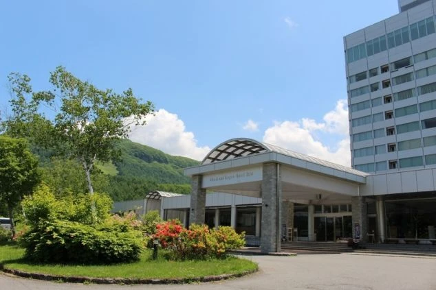 青空の下、緑豊かな山々を背景に立つホテルのエントランスと白い高層の建物。