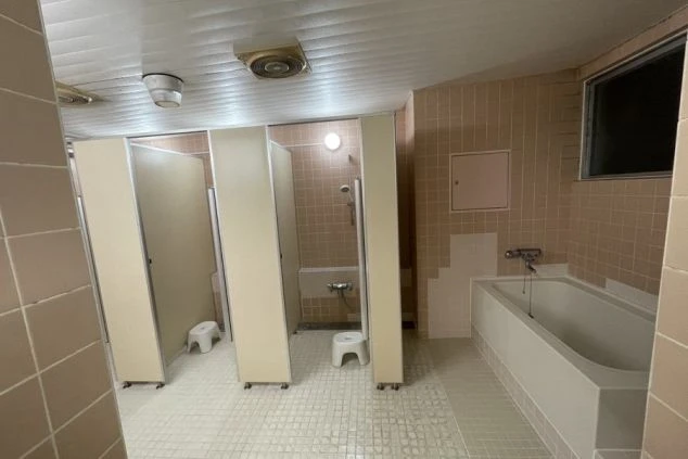 寮の共同浴場の画像。複数のシャワーブースと浴槽があり、ピンク色のタイルが特徴的。リゾートバイト中の入浴設備。