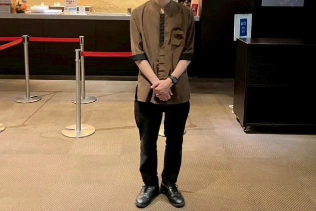 フロントで働く男性スタッフ。茶色いシャツに黒いパンツを着用した制服で、落ち着いた雰囲気を演出。