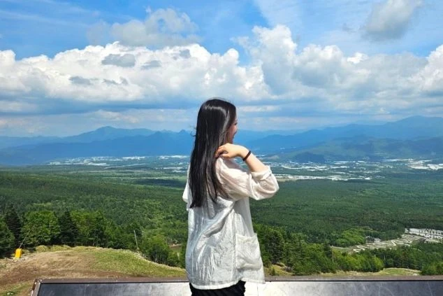 標高の高い展望スポットから、パノラマに広がる山々と街並みを眺める女性の後ろ姿。