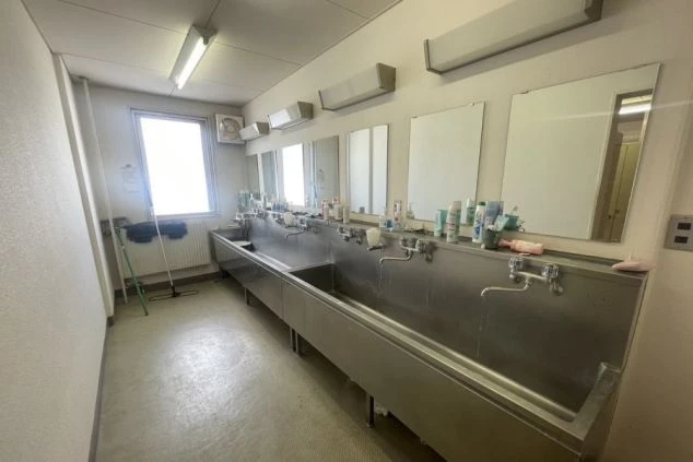 寮の共同洗面所の画像。複数のシンクと鏡が並び、窓からは明るい光が差し込む。リゾートバイト中の身だしなみに便利。