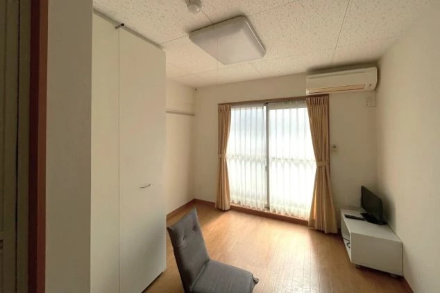 リゾートバイト寮の室内。フローリングの床で、テレビやエアコン、クローゼットが備え付けられている。明るく清潔感のある空間。