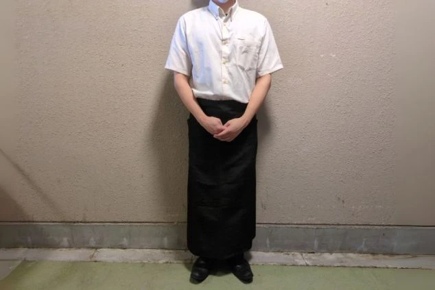 白い半袖シャツと黒いロングエプロンを着用した男性スタッフの画像。夏でも涼しく、動きやすい服装である。リゾートバイトの仕事内容を表す、レストランスタッフの制服の画像。