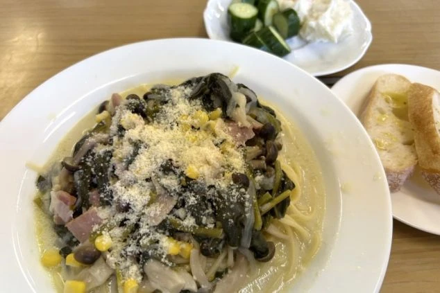 クリームソースのパスタ。付け合わせとして、バゲットとキュウリ、ポテトサラダが添えられている。