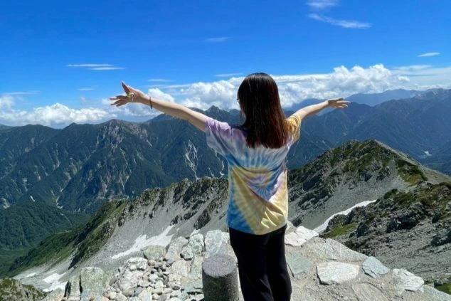 富山・弥陀ヶ原の絶景をバックに両手を広げる女性の画像。立山黒部アルペンルート周辺のリゾートバイトで体験できる山岳リゾートの休日。