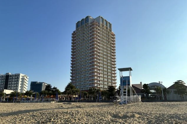 青空の下、サンセットビーチにそびえ立つ勤務先のホテル外観。海が目の前の絶好のロケーションで、沖縄のリゾートバイトを象徴する開放的な景色。