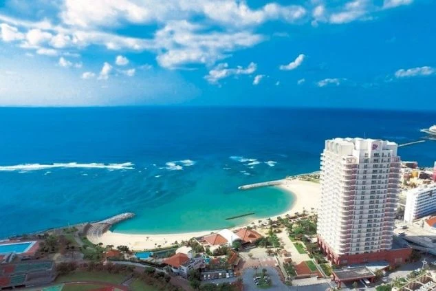 青空の下、サンセットビーチにそびえ立つ勤務先のホテル外観。海が目の前の絶好のロケーションで、沖縄のリゾートバイトを象徴する開放的な景色。