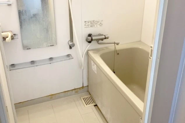 個室内に設置されたユニットバス。コンパクトな浴槽とシャワー、鏡、タオル掛けが備わっている。白を基調とした、清潔感のある一人用の入浴設備。